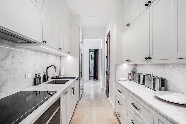 kitchen with sink, light stone counters, black electric cooktop, decorative backsplash, and white cabinets