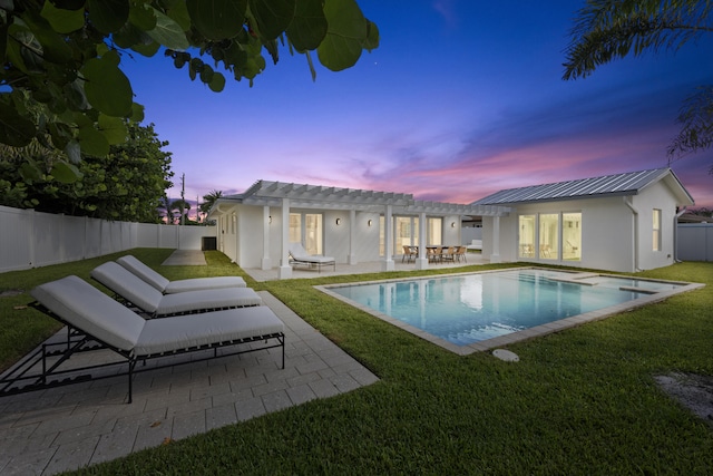 pool at dusk featuring a patio and a lawn