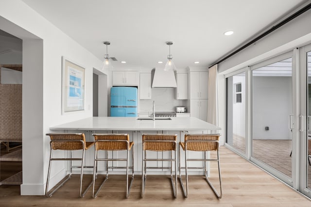 kitchen featuring sink, decorative light fixtures, light wood-type flooring, white cabinetry, and white fridge