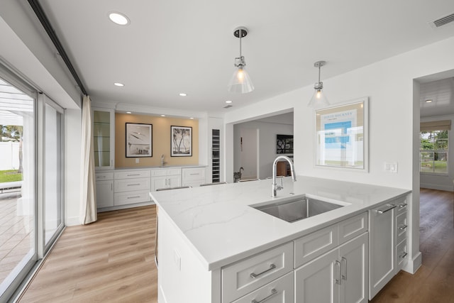 kitchen with sink, decorative light fixtures, light wood-type flooring, white cabinetry, and light stone counters