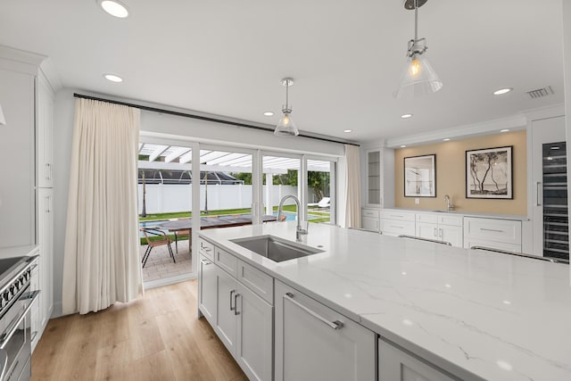 kitchen with sink, white cabinets, hanging light fixtures, and light hardwood / wood-style flooring