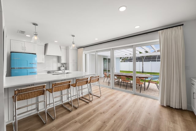 kitchen with stainless steel fridge, hanging light fixtures, premium range hood, white cabinetry, and light hardwood / wood-style flooring