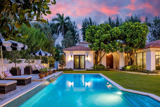 pool at dusk featuring a yard and a patio area