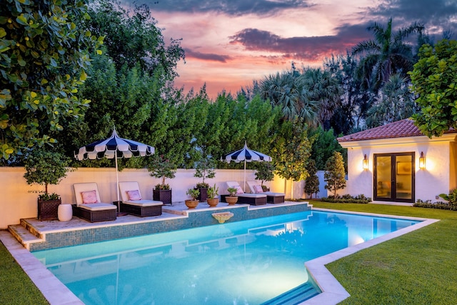 pool at dusk featuring outdoor lounge area, a yard, and a patio area