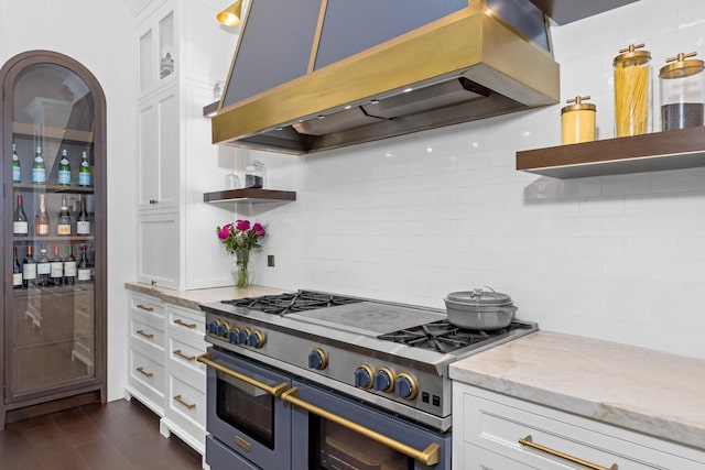 kitchen with white cabinetry, double oven range, exhaust hood, light stone countertops, and dark wood-type flooring