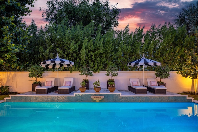 pool at dusk with a patio area and an outdoor hangout area