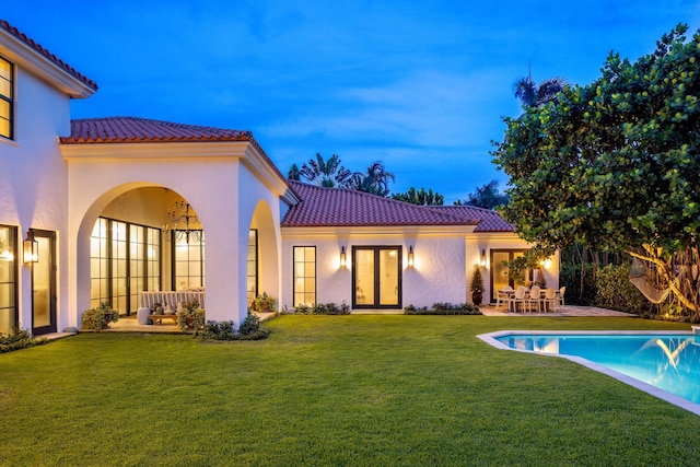 back house at dusk with a lawn and a patio