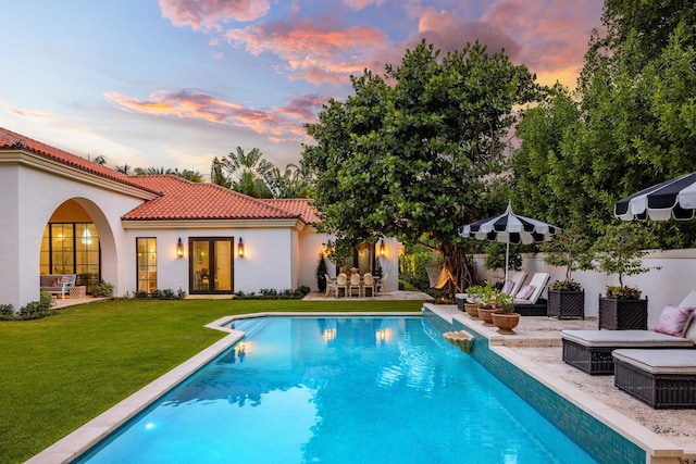 pool at dusk with a lawn and a patio