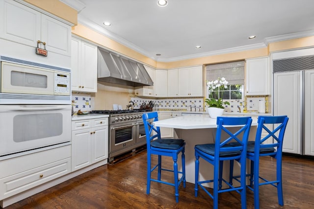 kitchen featuring white appliances, wall chimney range hood, white cabinets, a center island, and dark hardwood / wood-style floors