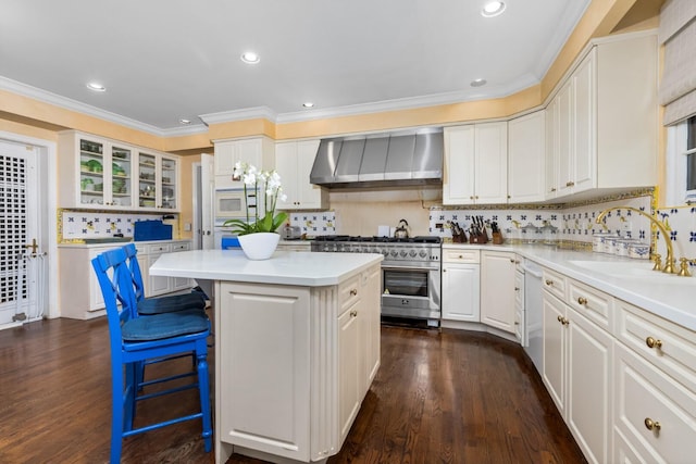 kitchen with decorative backsplash, white appliances, a kitchen island, and wall chimney range hood