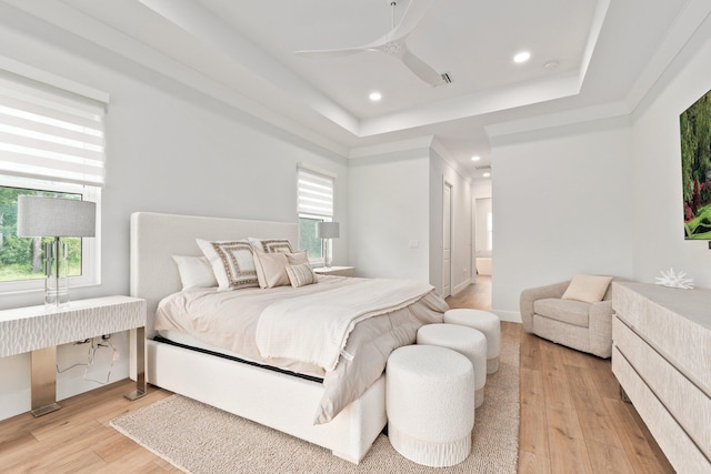 bedroom featuring ceiling fan, a raised ceiling, ensuite bathroom, and light hardwood / wood-style flooring