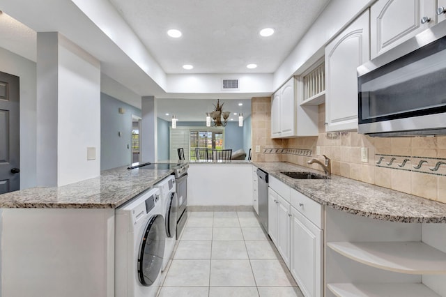 kitchen with appliances with stainless steel finishes, washer / clothes dryer, kitchen peninsula, sink, and light stone counters