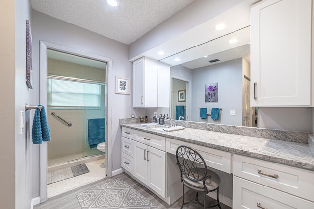 bathroom featuring vanity, a textured ceiling, wood-type flooring, a shower with door, and toilet