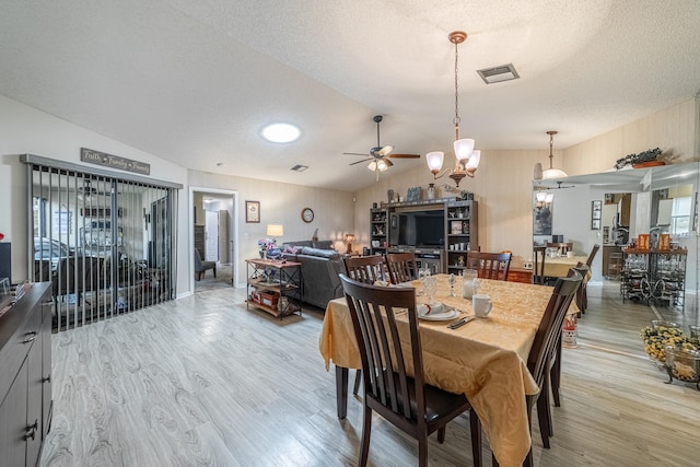 dining area with a textured ceiling, ceiling fan with notable chandelier, light hardwood / wood-style floors, and vaulted ceiling