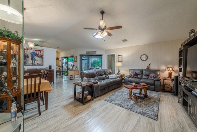 living room with ceiling fan, a textured ceiling, light hardwood / wood-style floors, and vaulted ceiling