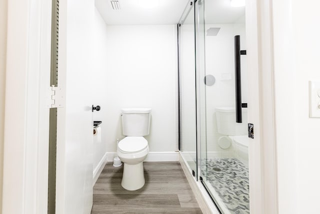 bathroom with hardwood / wood-style floors, a shower with shower door, and toilet