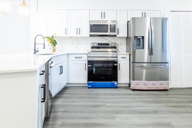 kitchen with appliances with stainless steel finishes, white cabinetry, pendant lighting, light hardwood / wood-style flooring, and sink