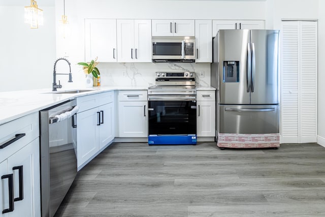 kitchen featuring light stone counters, white cabinets, sink, decorative light fixtures, and appliances with stainless steel finishes