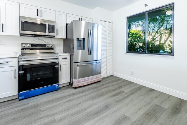 kitchen with light stone counters, light hardwood / wood-style flooring, stainless steel appliances, and white cabinetry