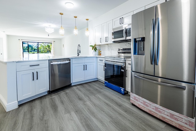 kitchen featuring appliances with stainless steel finishes, hanging light fixtures, white cabinets, light wood-type flooring, and sink