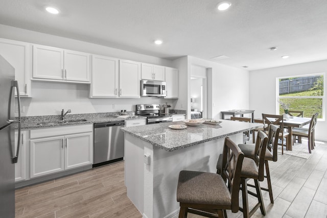 kitchen with sink, appliances with stainless steel finishes, a kitchen breakfast bar, light stone countertops, and white cabinets