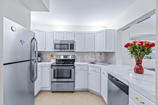 kitchen with light stone countertops, stainless steel appliances, white cabinetry, sink, and tasteful backsplash