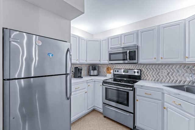 kitchen featuring light tile patterned floors, white cabinetry, backsplash, and stainless steel appliances