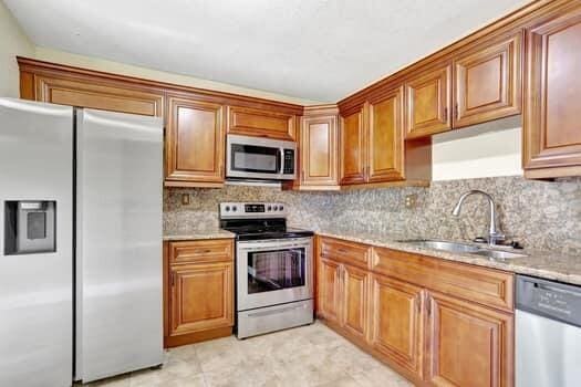 kitchen with light stone counters, stainless steel appliances, tasteful backsplash, and sink