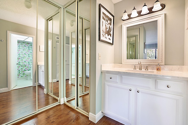 bathroom with a textured ceiling, vanity, toilet, and hardwood / wood-style flooring