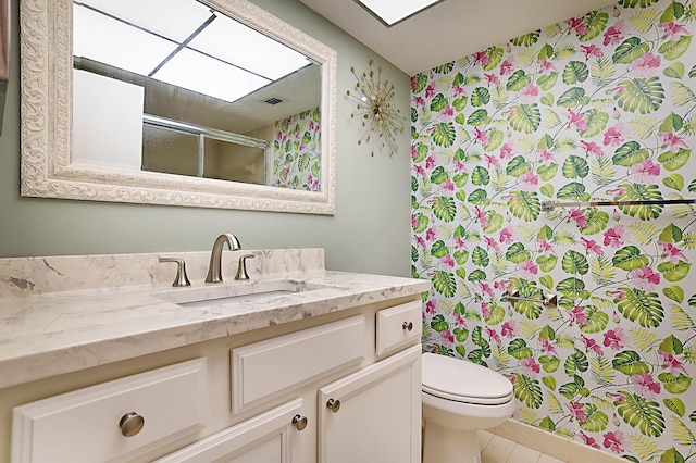 bathroom with a shower with door, vanity, toilet, and tile patterned floors