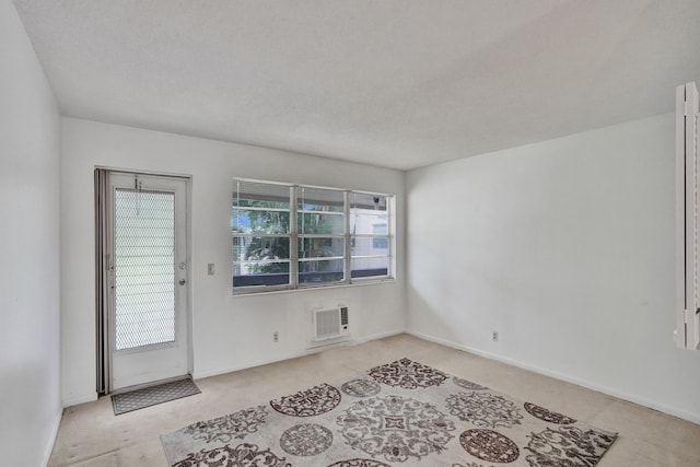 unfurnished room featuring a wall mounted AC, a textured ceiling, and light colored carpet