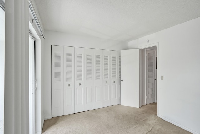 unfurnished bedroom featuring a textured ceiling, a closet, and light carpet