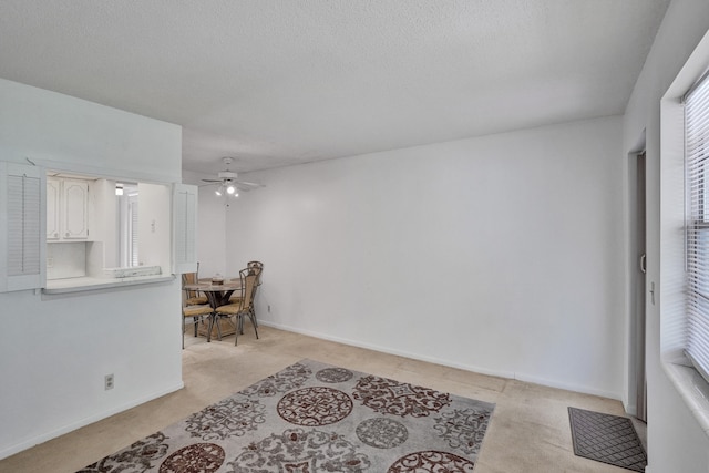 interior space with a textured ceiling, light colored carpet, and ceiling fan