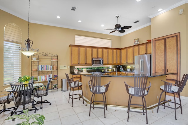 kitchen with crown molding, stainless steel appliances, ceiling fan, pendant lighting, and a breakfast bar