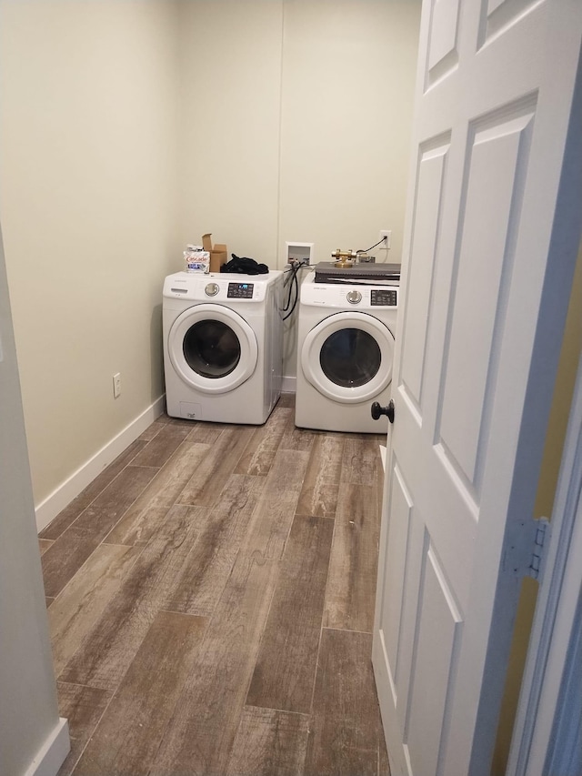 clothes washing area featuring washing machine and clothes dryer, laundry area, baseboards, and wood finished floors