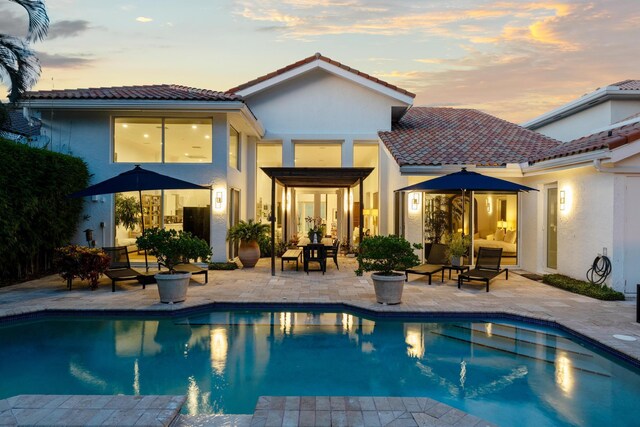 pool at dusk featuring an in ground hot tub, a patio area, and a lawn