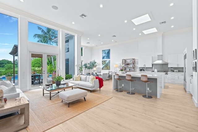 living room with a skylight, light hardwood / wood-style floors, crown molding, french doors, and a high ceiling