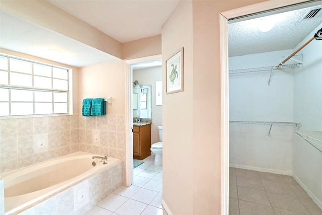 bathroom with tile patterned floors, toilet, vanity, a relaxing tiled tub, and a textured ceiling