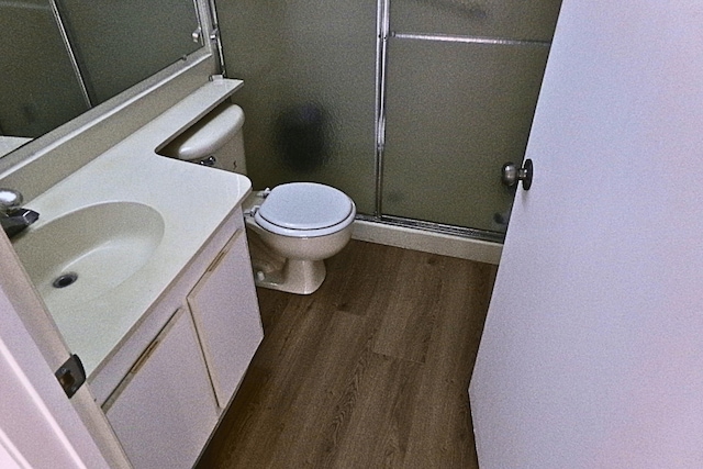 bathroom with hardwood / wood-style flooring, vanity, an enclosed shower, and toilet