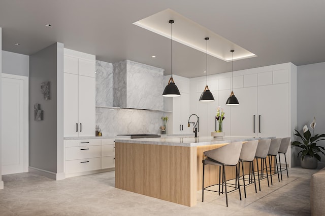 kitchen with decorative backsplash, a kitchen island with sink, white cabinets, hanging light fixtures, and a breakfast bar area