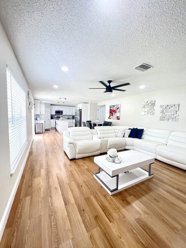 living room with ceiling fan, light hardwood / wood-style flooring, and a textured ceiling