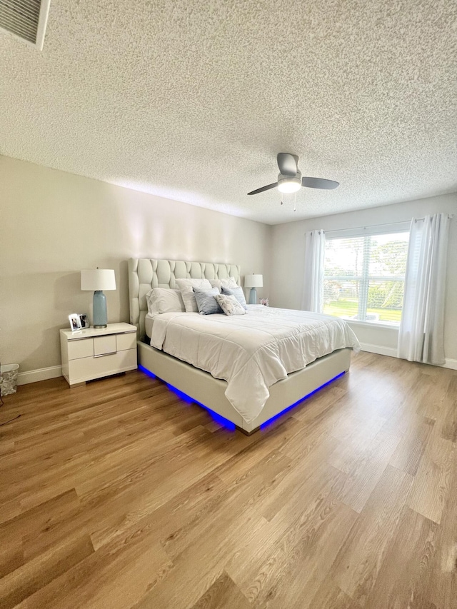 bedroom with ceiling fan, a textured ceiling, and light wood-type flooring