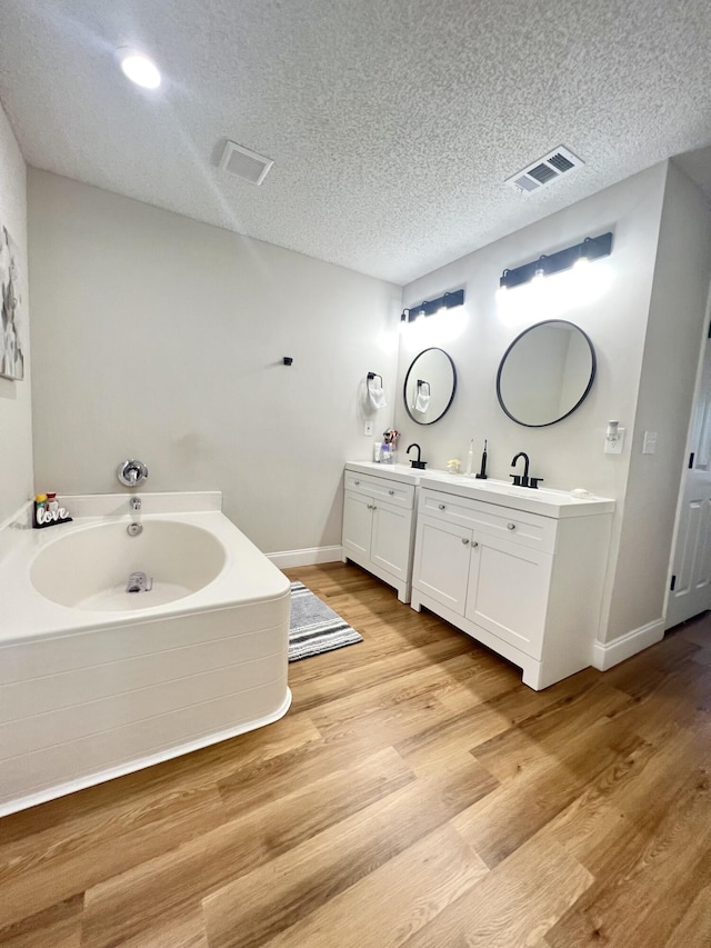 bathroom with a tub to relax in, vanity, hardwood / wood-style flooring, and a textured ceiling