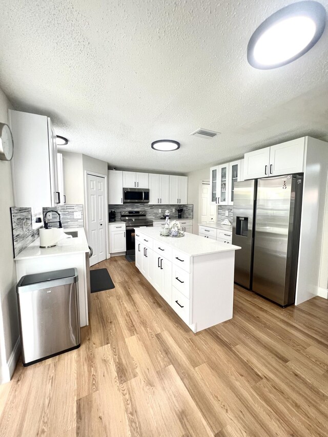 kitchen with white cabinets, decorative backsplash, light hardwood / wood-style floors, and appliances with stainless steel finishes