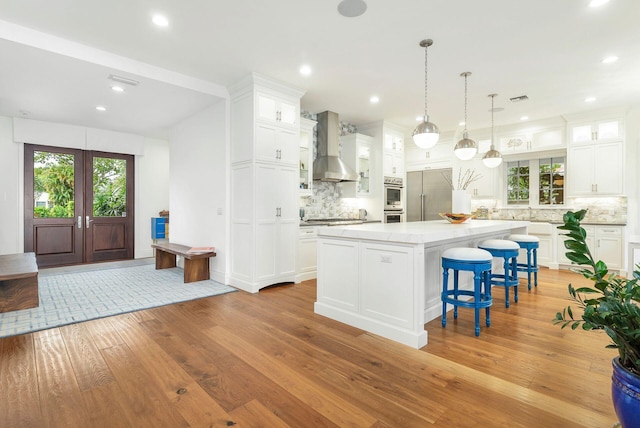 kitchen with light hardwood / wood-style flooring, a center island, appliances with stainless steel finishes, white cabinets, and wall chimney range hood