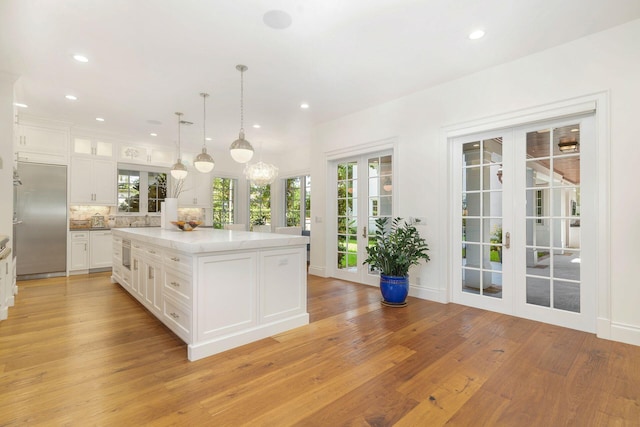 kitchen featuring white cabinets, hanging light fixtures, a center island, light wood-type flooring, and built in refrigerator