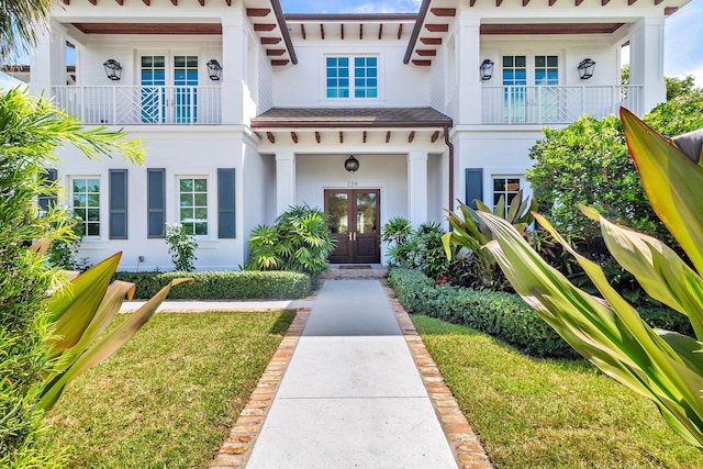 doorway to property featuring a balcony, a lawn, and french doors