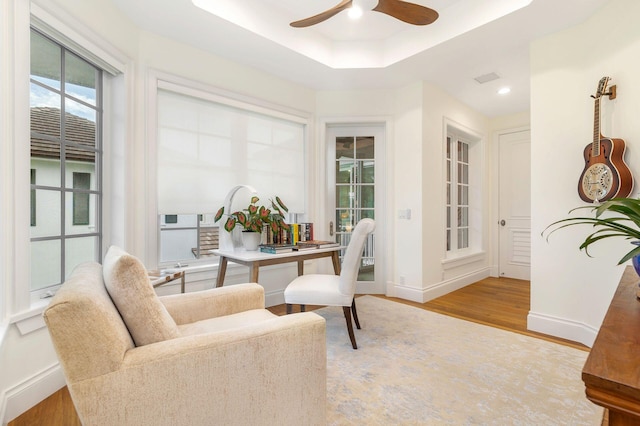 living area featuring a raised ceiling, hardwood / wood-style floors, and ceiling fan