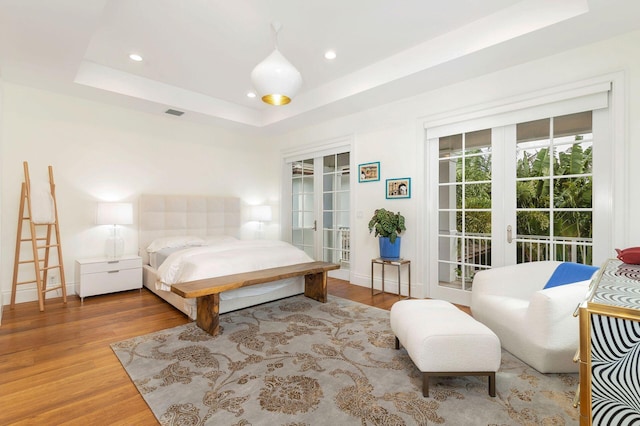 bedroom with a raised ceiling, wood-type flooring, french doors, and access to outside