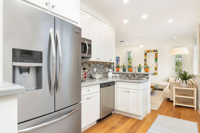 kitchen with light hardwood / wood-style flooring, appliances with stainless steel finishes, white cabinetry, sink, and kitchen peninsula